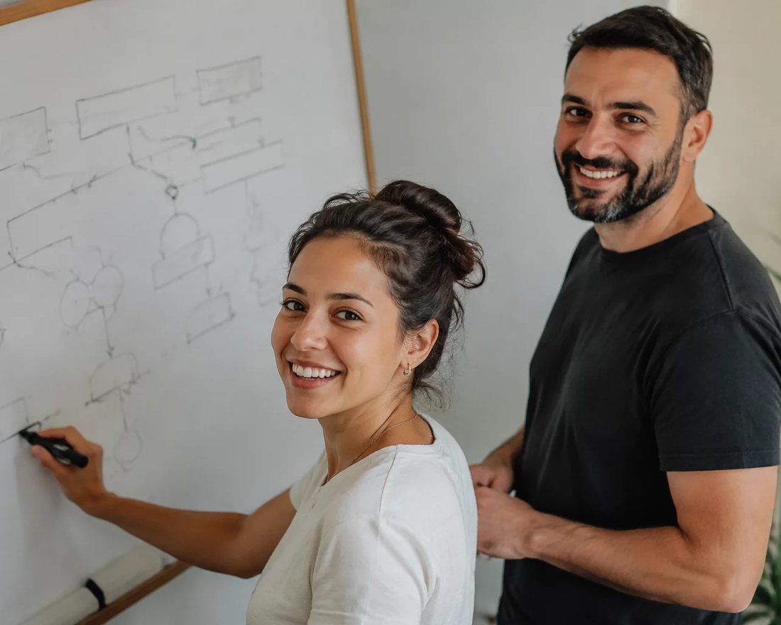 Duas pessoas em pé diante de um quadro branco onde um argumento está desenhado